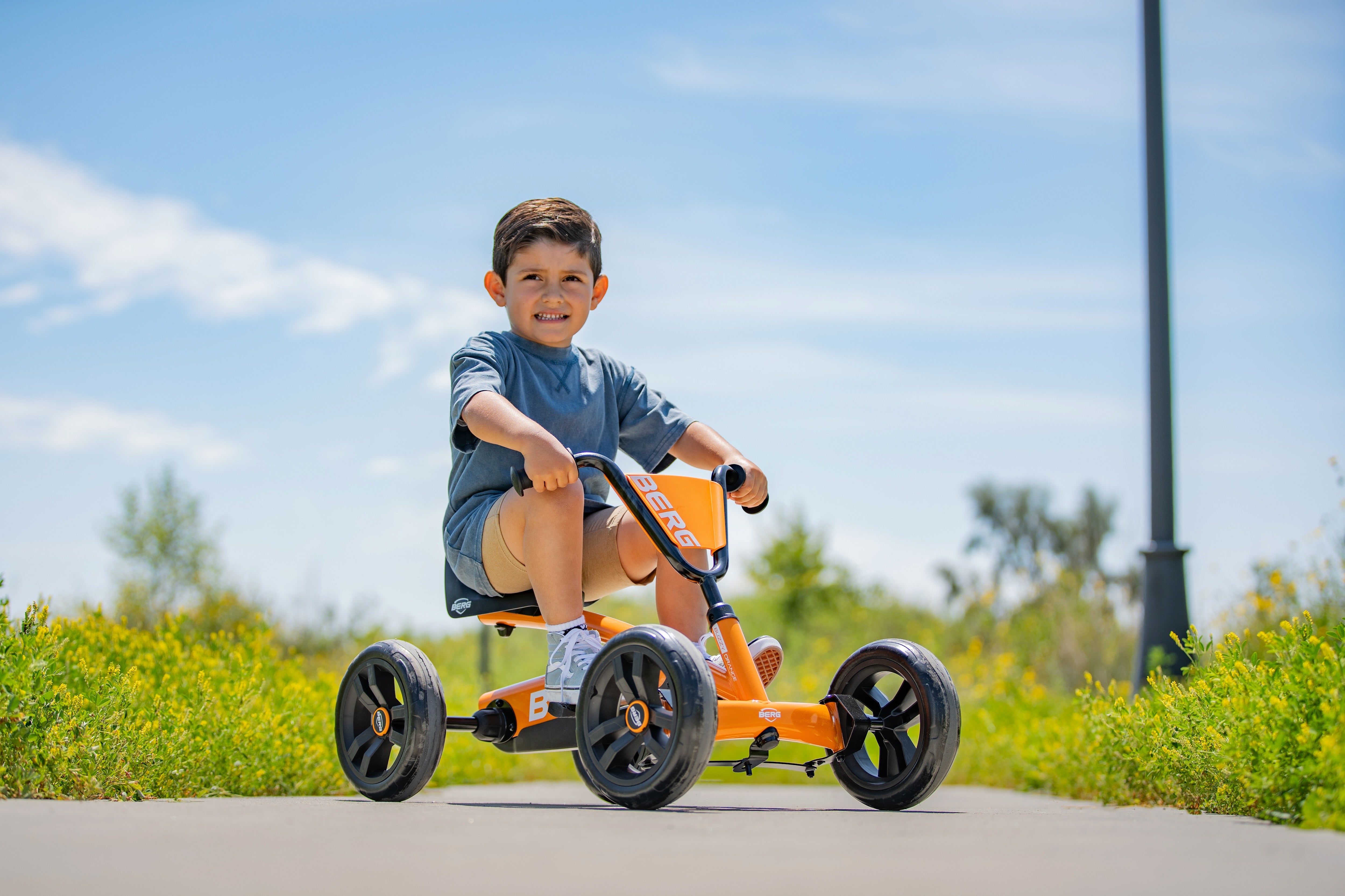 Child riding the BERG Buzzy orange pedal go-kart outdoors